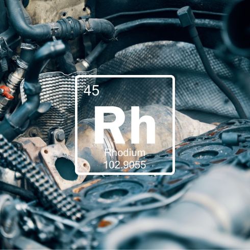 Rhodium (Rh) chemical element graphic over recycled automotive engine components, highlighting precious metal recovery.